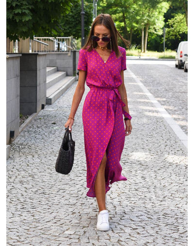femme portant une robe de plage fuchsia à pois orange, style chic décontracté, sac noir et baskets blanches sur rue pavée ensoleillée