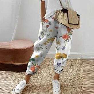 Femme portant un pantalon décontracté uni blanc avec motifs floraux colorés, style confortable et casual.