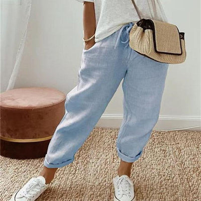 Femme portant un pantalon décontracté uni bleu clair en tissu léger, avec poches, lacet à la taille, et baskets blanches, sac beige en bandoulière.