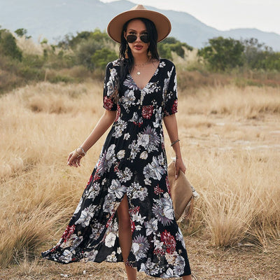 Femme portant une robe d'été fleurie noire à motifs floraux blancs et rouges avec chapeau beige en plein air dans un champ sec.
