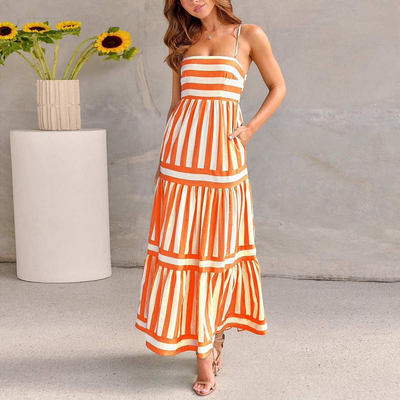 Femme portant une robe longue à bretelles rayée orange et blanche style plage, ambiance élégante et estivale.