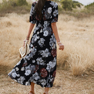 Femme portant une robe d'été fleurie noire à motifs blancs et bordeaux en plein air, style bohème élégant et léger.